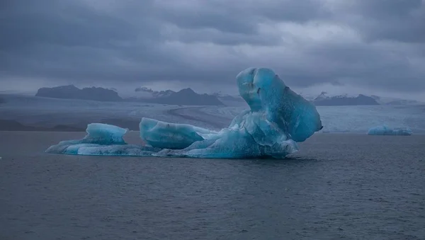 Velká mohyla ledovcového ostrova uprostřed oceánu s zamračenou oblohou pozadí — Stock fotografie