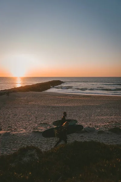 Schöne Aussicht auf den Strand mit zwei Surfern am Ufer bei Sonnenuntergang — Stockfoto