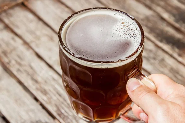 Persoon met een glazen kop koud bier met een houten ondergrond op de achtergrond — Stockfoto