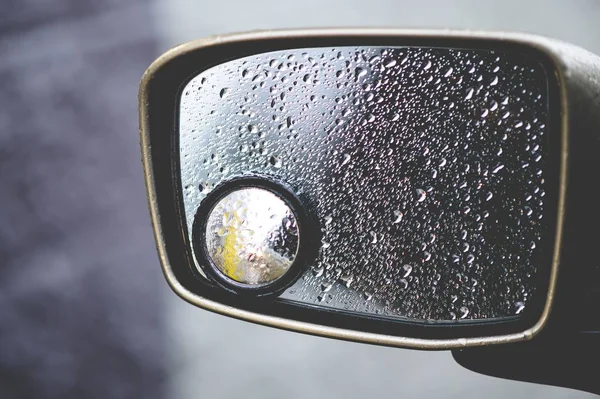 Encerramento de um espelho retrovisor coberto de gotas de chuva sob a luz do sol com um fundo borrado — Fotografia de Stock