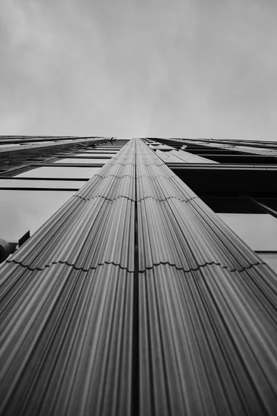 Low angle greyscale of a modern skyscraper under the cloudy sky — Stock Photo, Image