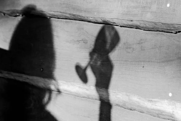 A grayscale hot of a person shadow holding a wine glass over a wooden surface