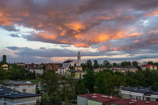 Foto panorámica de una pequeña ciudad con una iglesia en el centro bajo un cielo nublado naranja. —  Fotos de Stock