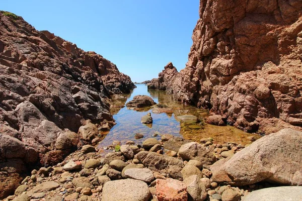 Landscape shot of a seashore surrounded with big rocks on each side in a clear blue sky — Stock Photo, Image