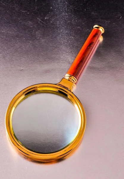 High angle shot of a golden magnifying glass laid on a silver surface — Stock Photo, Image