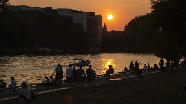 Park med människor som går runt nära en flod med solen i bakgrunden — Stockfoto