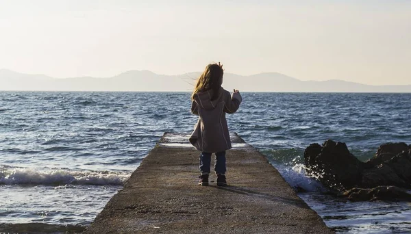 Lange Aufnahme eines kleinen Mädchens, das auf einem Steg am felsigen Meer steht — Stockfoto