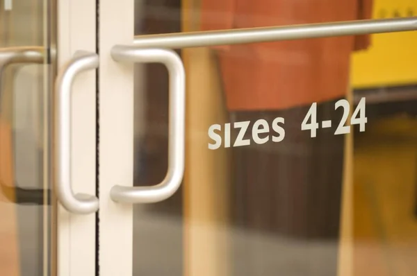 Närbild av en dörr i butiken med storlekarna 4-24 skrivna på den under solljuset — Stockfoto