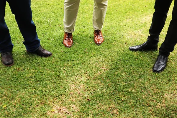 Hochwinkelschuss von drei männlichen Füßen, die auf dem grasbedeckten Feld stehen — Stockfoto