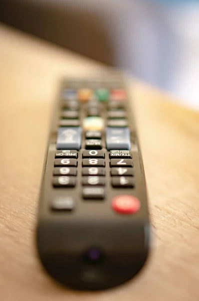 Vertical closeup shot of a remote controller on a wooden surface with a blurred background — Stock Photo, Image