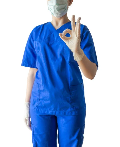 Ung framgångsrik kvinnlig läkare i en blå medicinsk uniform och en mask som visar okej tecken — Stockfoto