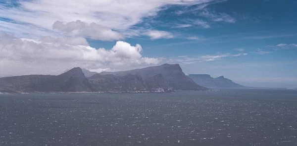 Wide shot of an open sea with mountains and a cloudy blue sky in the background — Stock Photo, Image