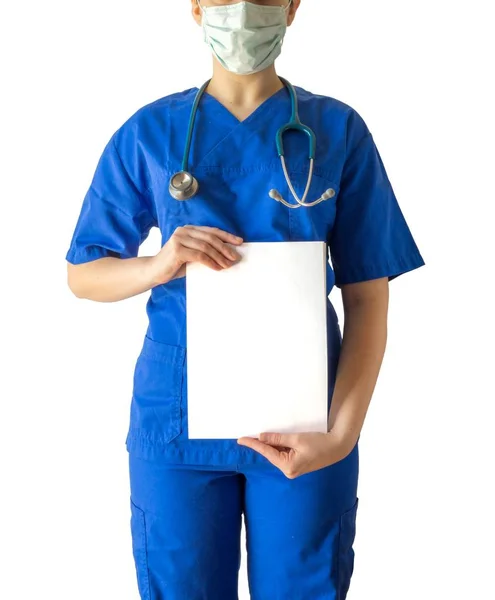 Médico feminino em um uniforme médico azul e máscara segurando um papel branco em branco com um espaço de cópia — Fotografia de Stock