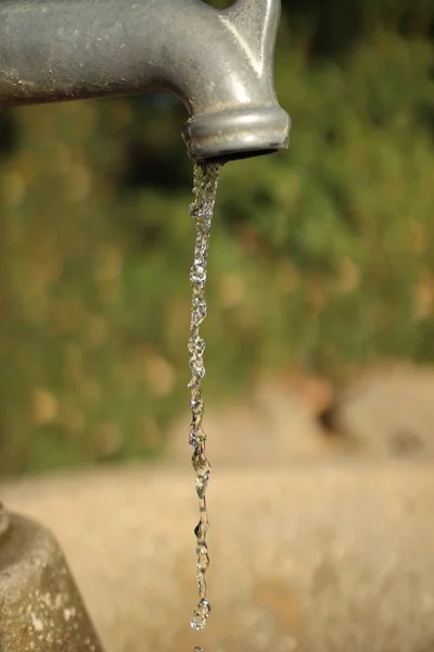 Fermer la prise de vue verticale d'un robinet gris égouttant de l'eau avec un flou en arrière-plan — Photo