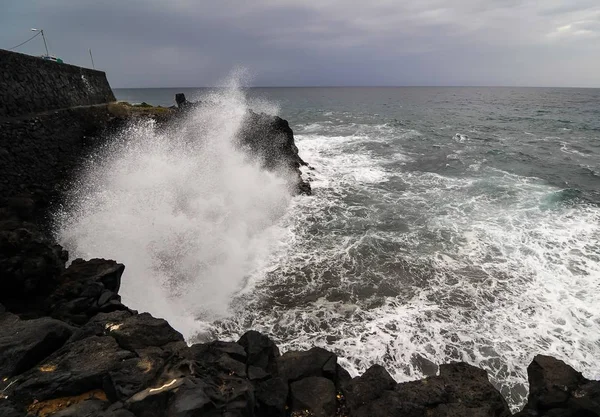 Alto ángulo disparado de fuertes olas de mar golpeando las rocas con un cielo sombrío en el fondo. — Foto de Stock