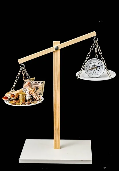 Vertical shot of a balancing scale balances money and compass with a pitch-black background — Stock Photo, Image