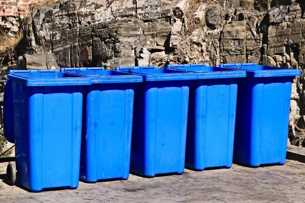 Encerramento tiro de uma linha de latas de lixo azul na frente de uma formação rochosa — Fotografia de Stock