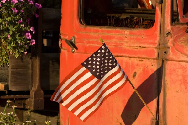 US flag on an old rusty red van surrounded by flowers under the sunlight