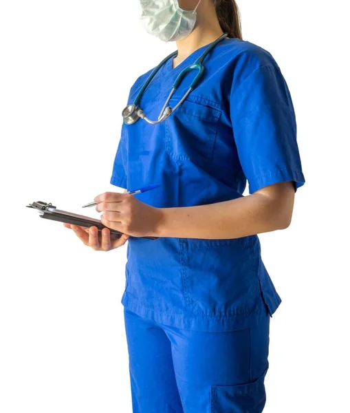 Médico jovem em um uniforme médico azul e uma máscara tomando notas em um caderno — Fotografia de Stock