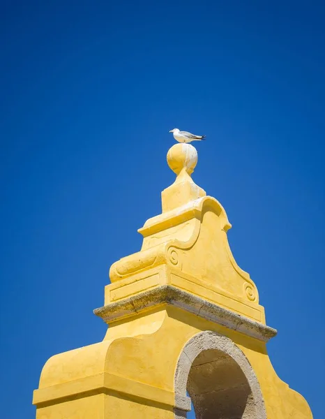 Niski kąt strzału mewy siedzącej na szczycie żółtej wieży pod przejrzystym błękitnym niebem — Zdjęcie stockowe