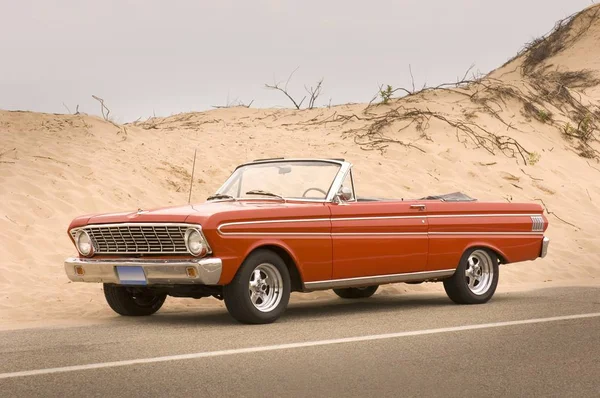 Red convertible car on the road surrounded by hills covered in the sand — 스톡 사진