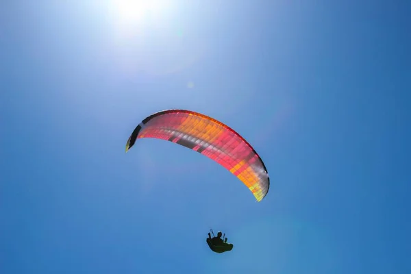 Baixo ângulo tiro de uma pessoa parapente em um dia ensolarado sob o céu brilhante — Fotografia de Stock