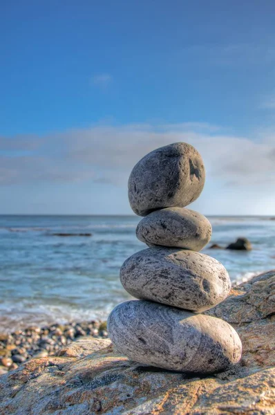 Arka planda bulanık mavi gökyüzü olan deniz kıyısındaki istiflenmiş taşların seçici odak noktası. — Stok fotoğraf