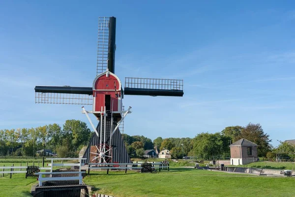 Molino de viento bajo un cielo azul claro rodeado de árboles y vegetación —  Fotos de Stock