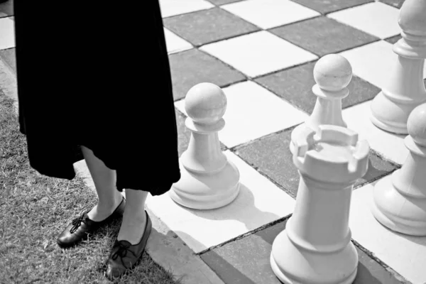 Balança cinza de uma fêmea usando um vestido preto em pé por um grande tabuleiro de xadrez — Fotografia de Stock