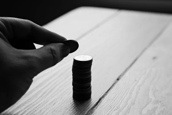 Escala cinza close-up tiro de uma pessoa colocando algumas moedas em uma coluna em uma mesa de madeira — Fotografia de Stock