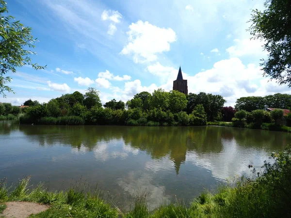 Paesaggio di un lago circondato da alberi verdi con un edificio in un cielo nuvoloso blu — Foto Stock