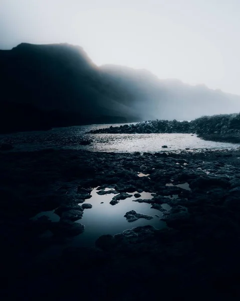 Pionowe ujęcie z czarnych kamieni otaczających jezioro w ponury dzień — Zdjęcie stockowe