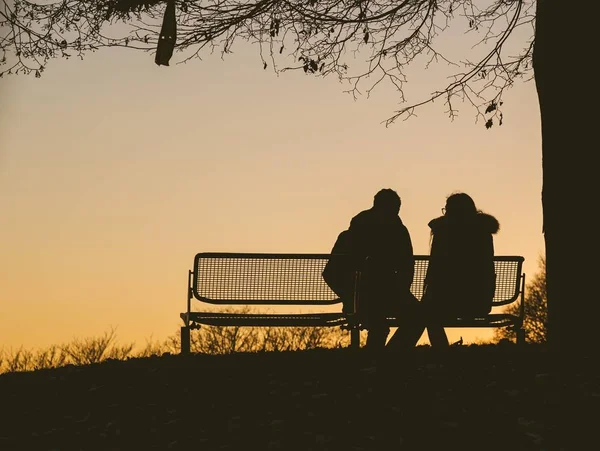 Silhouette of two people sitting on a bench under a tree during a sunset — Stock Photo, Image