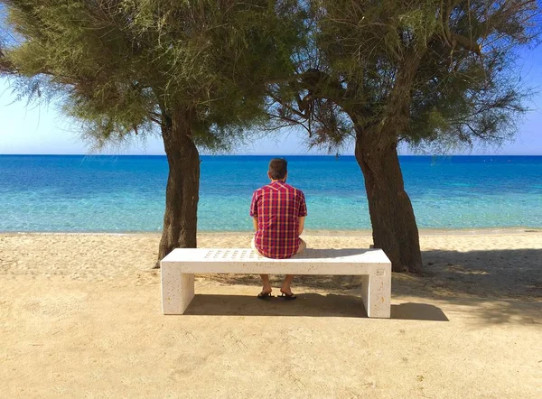 Belle photo d'un homme portant une chemise à carreaux, assis sur un banc blanc — Photo