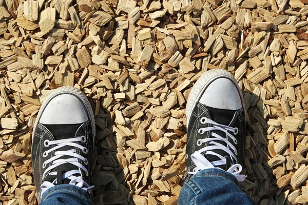 Colpo ad angolo alto dei piedi di una persona in piedi sul terreno coperto con costolette di legno — Foto Stock