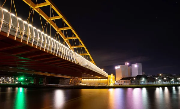 Puente en una ciudad con un gran arco amarillo en la cima por la noche. — Foto de Stock