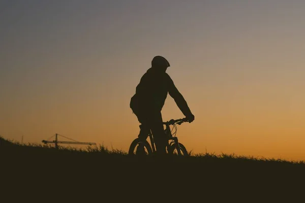 Silhouette of a person riding a bike on a field during a sunset — Foto de Stock