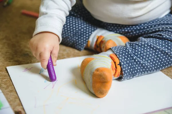 Babysitten op de vloer en tekenen op een wit papier met een paars krijtje — Stockfoto