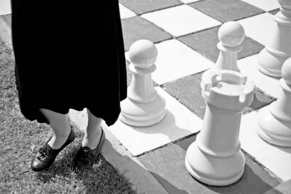 Серый снимок женщины в черном платье, стоящей у большой шахматной доски — стоковое фото