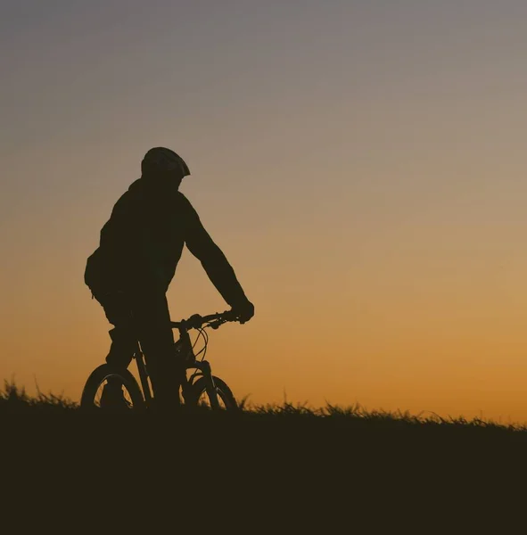 Silhouette einer Person, die bei Sonnenuntergang mit dem Fahrrad auf einem Feld fährt — Stockfoto