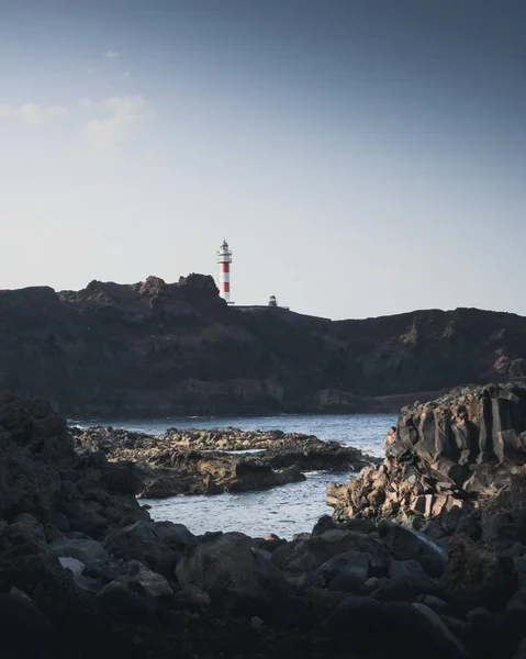 Denizin kayalık kıyılarının dik açılı görüntüsü ve arka planda bir deniz feneri. — Stok fotoğraf