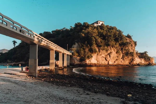 Pláž obklopená mořem a skalami pokrytá zelení s mostem v Brazílii — Stock fotografie
