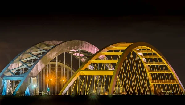 Mosty ve městě s velkými žlutými a bílými oblouky na vrcholu v noci — Stock fotografie