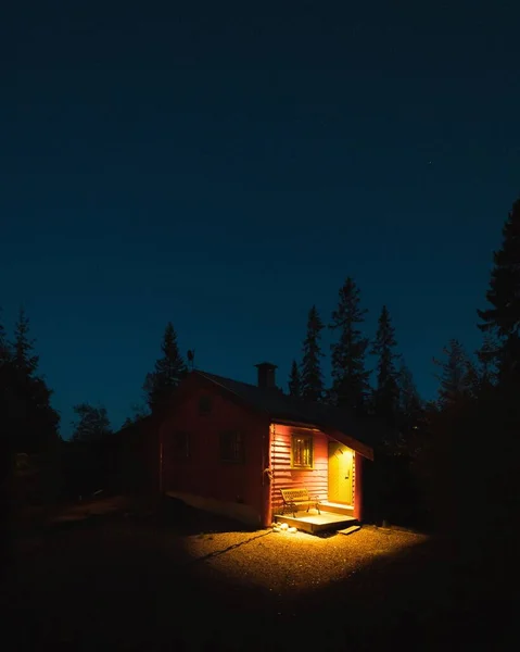 Photo verticale d'une cabane éclairée dans une forêt entourée de nombreux arbres la nuit en Norvège — Photo