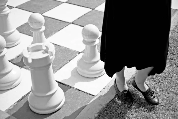 Grey scale shot of a female wearing a black dress standing by a big chess board — Stock Photo, Image