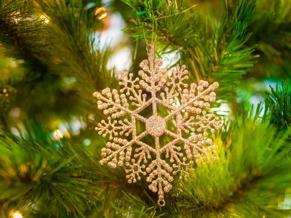 Närbild av en snöflinga prydnad på julgranen under lamporna med en suddig bakgrund — Stockfoto