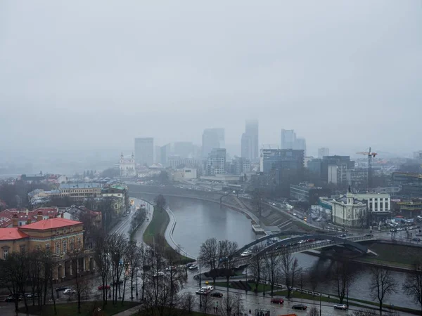 Bird\'s eye view of a foggy city with beautiful buildings and a bridge over a river