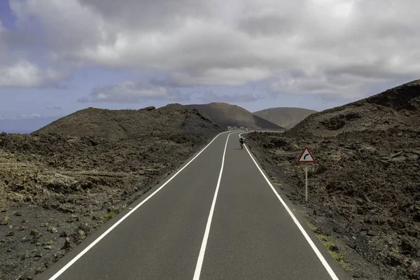 Görbe út körül dombok alatt felhős ég Timanfaya Nemzeti Park Spanyolországban — Stock Fotó