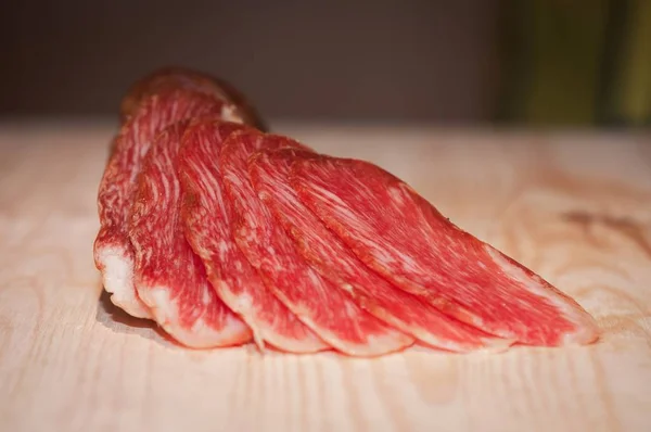 Primer plano de carne roja en rodajas sobre una superficie de madera con un fondo borroso —  Fotos de Stock