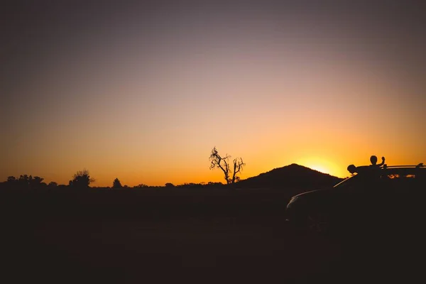 Silhouette d'une voiture avec des personnes entourées de verdure pendant le coucher de soleil doré — Photo